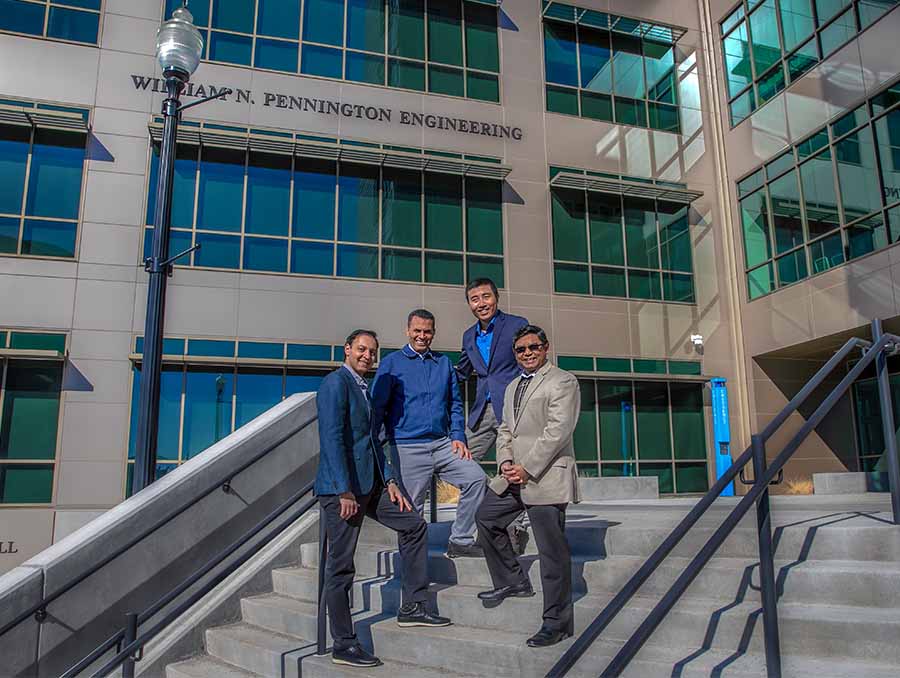 Four men standing on an outdoor stairwell in front of the Pennington Engineering Building.