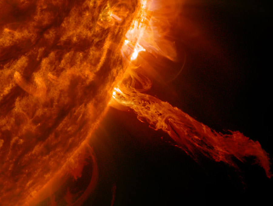 The sun takes up much of the left side of the image, but a large stream of plasma that looks like fire is extending out toward the right side of the photo.