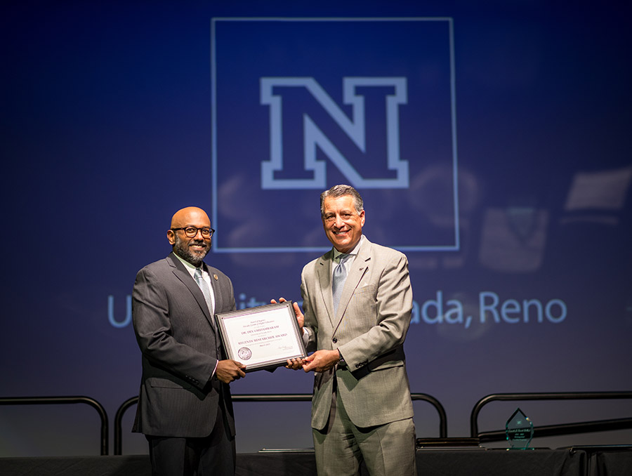 Two men, Dev Chidambaram on left, Brian Sandoval on right, holding framed award and looking at the camera.