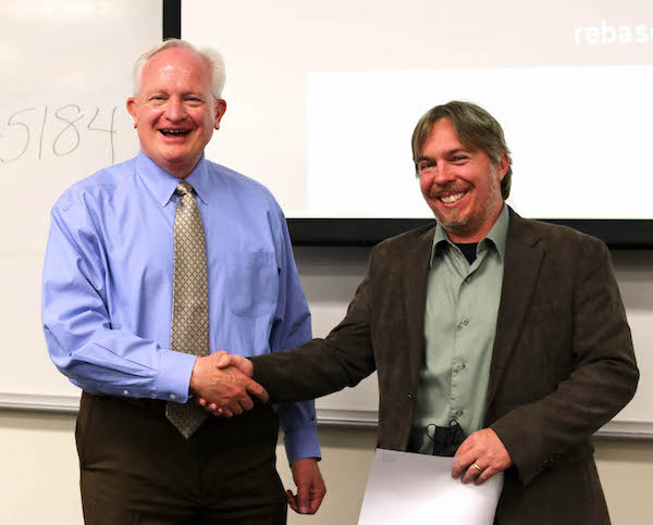 Provost Jeff Thompson smiles and shakes hands with Professor Chris Church in a classroom.
