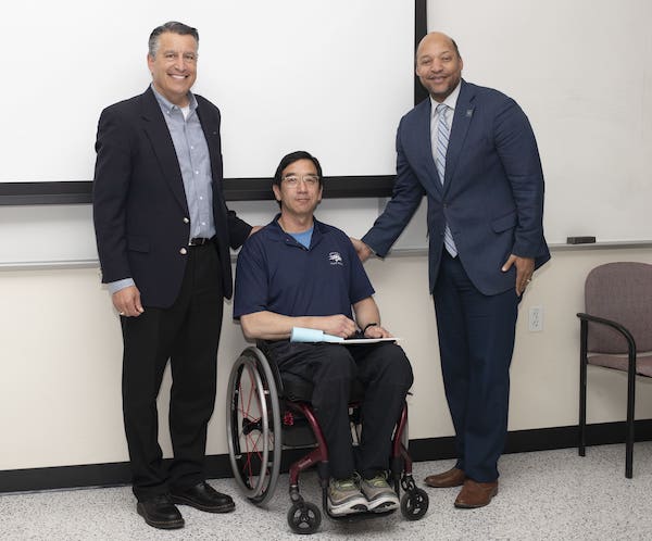 President Brian Sandoval, Professor Eric Wang, and College of Engineering Dean Jones smile for the camera as Wang holds the award certificate.