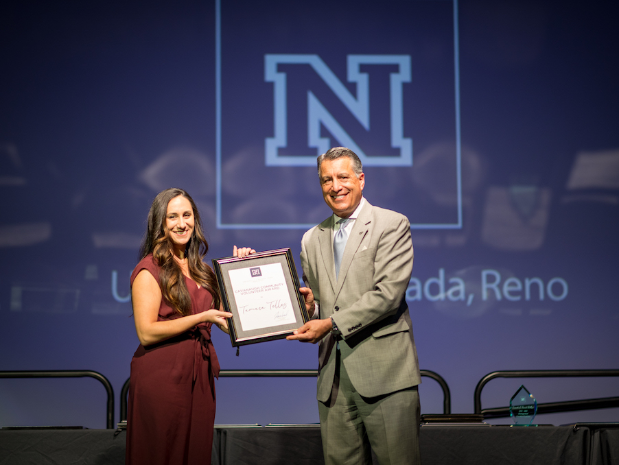 Tamara Telles smiles and holds a certificate on stage with University President Brian Sandoval.