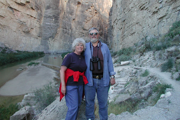 A woman and man stand in a canyon. The man has binoculars around his neck.