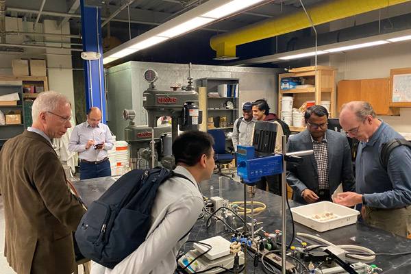 Seven people stand around a table in a research lab. They are looking at minerals and talking with one another.