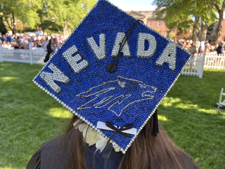 A bedazzled, sparkling graduation cap as viewed from behind with the Nevada Sport Wolf and the Nevada Blue colors with "Nevada" written in Silver gems and a little pretend diploma at the bottom.