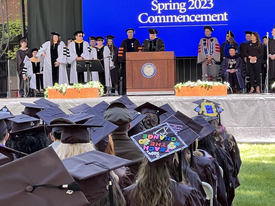 Provost Jeff Thompson at the podium speaking to the graduates who are listening on a sunny day in the quad.