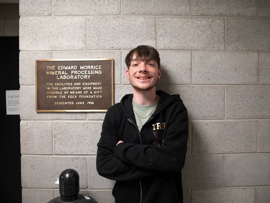 Tristan Morrice leans against a wall next to a plaque that reads, "The Edward Morrice Mineral Processing Laboratory."