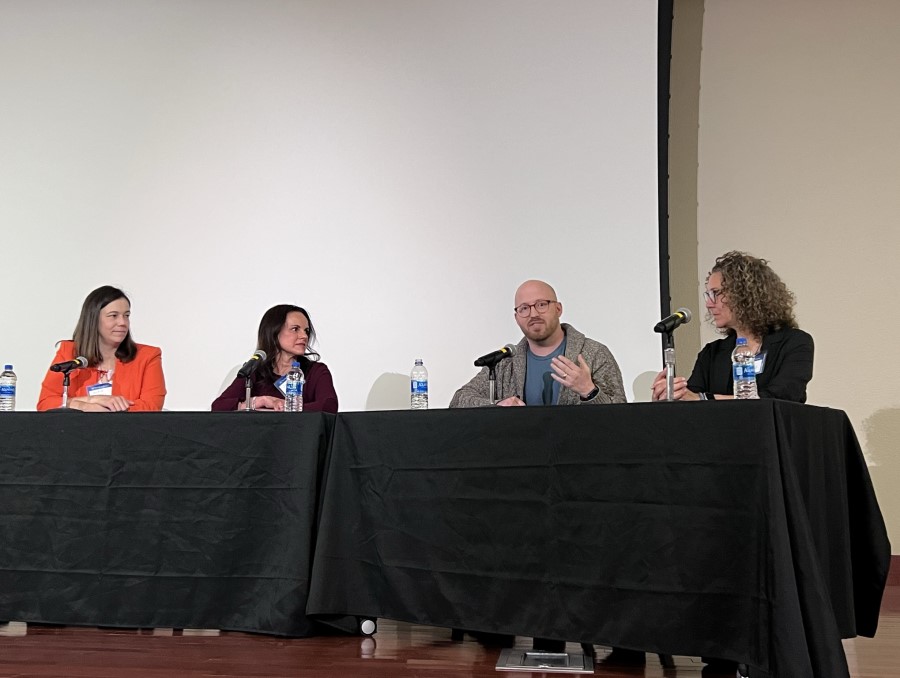 Event speakers Nicole Beaulieu, Jodi Patton, Bob Whitefield and Jackie Zuker sitting on stage at a long table covered by a black tablecloth.