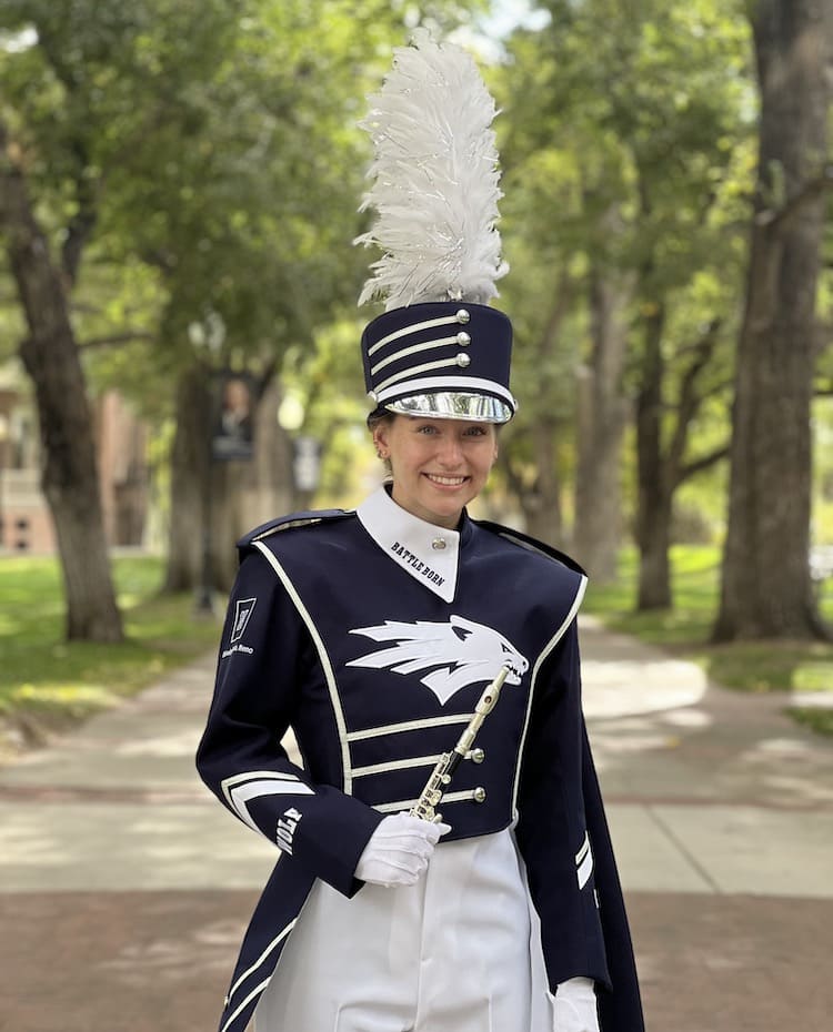 Woman smiling in a blue marching band uniform on a path in between two grass areas. 