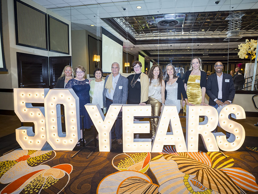 A group of people stand behind a large lit sign that reads "50 Years" in a hotel ballroom.