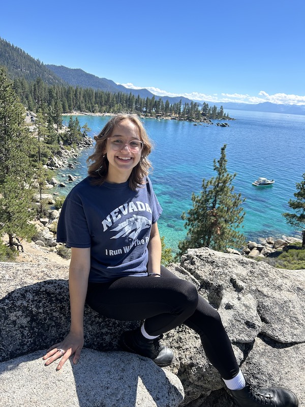 Anna Bachvarov sits on a rock overlooking Lake Tahoe while wearing a Nevada Wolf Pack t-shirt.