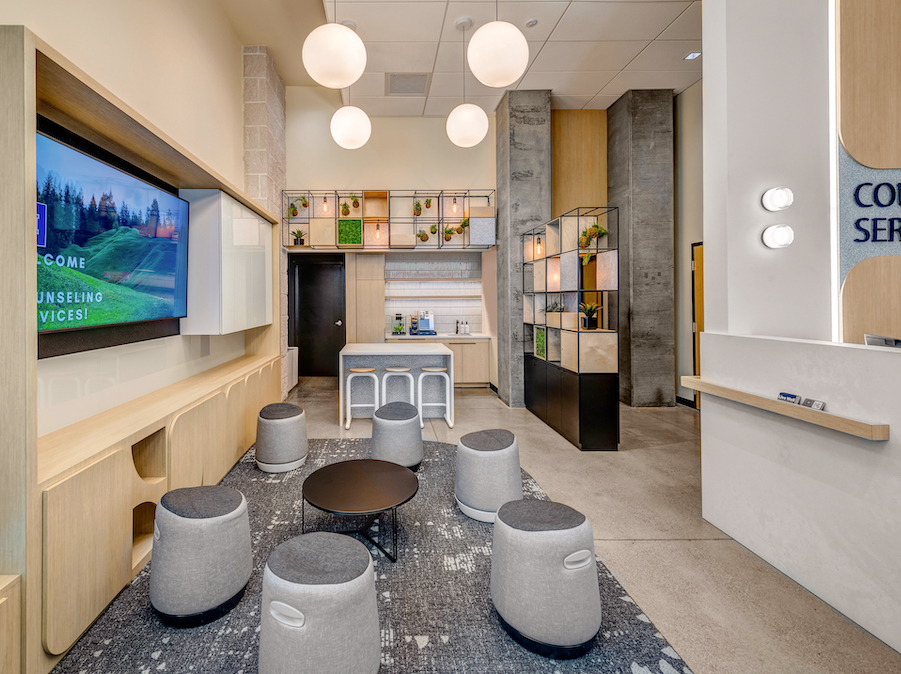 Interior of the Counseling Services Annex which has a number of stools and seats with hanging lights and a digital display screen.