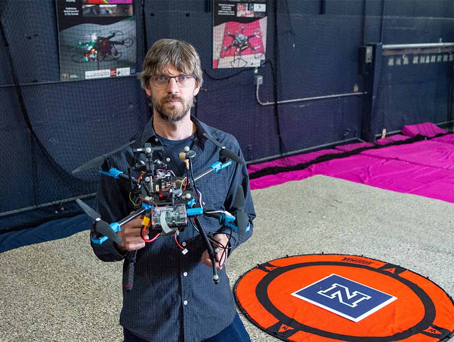 Floris van Breugel standing in a room holding a drone in his right hand.