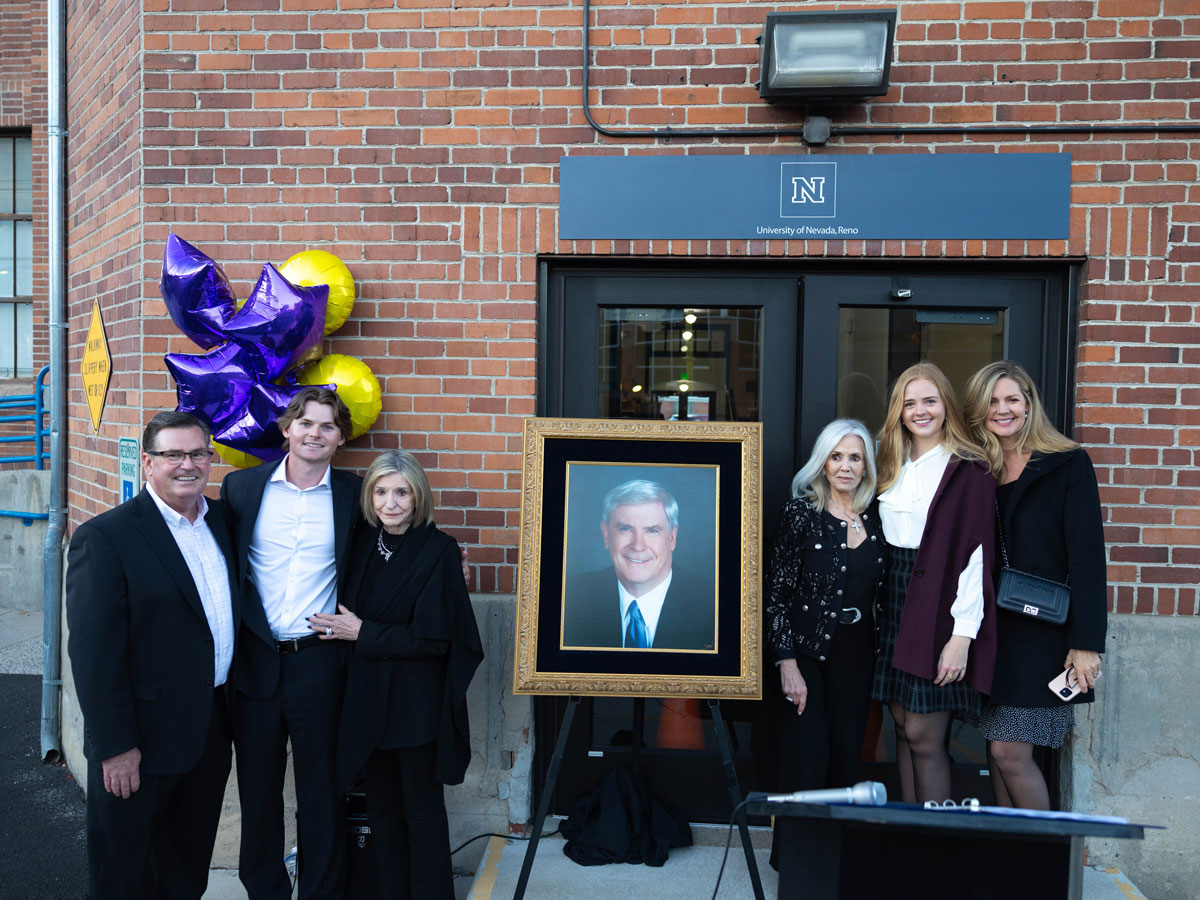 A group poses for a photo standing next to a portrait of Governor Kenny Guinn.