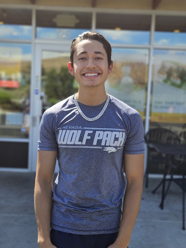 Jeferson Cordova stands smiling outside of the fitness center on campus while wearing a Nevada Wolf Pack t-shirt.