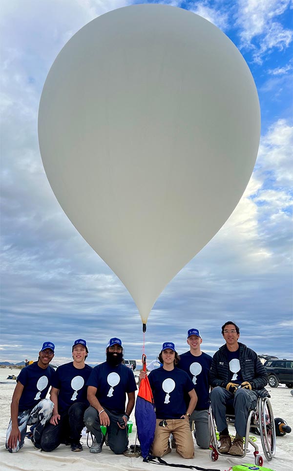 Six people, one in a wheelchair, stand with a scientific balloon in the desert.