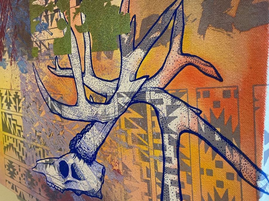 A mural with a depiction of a deer skull with large antlers on a yellow and orange background and a few blue/grey tribal designs overtop.