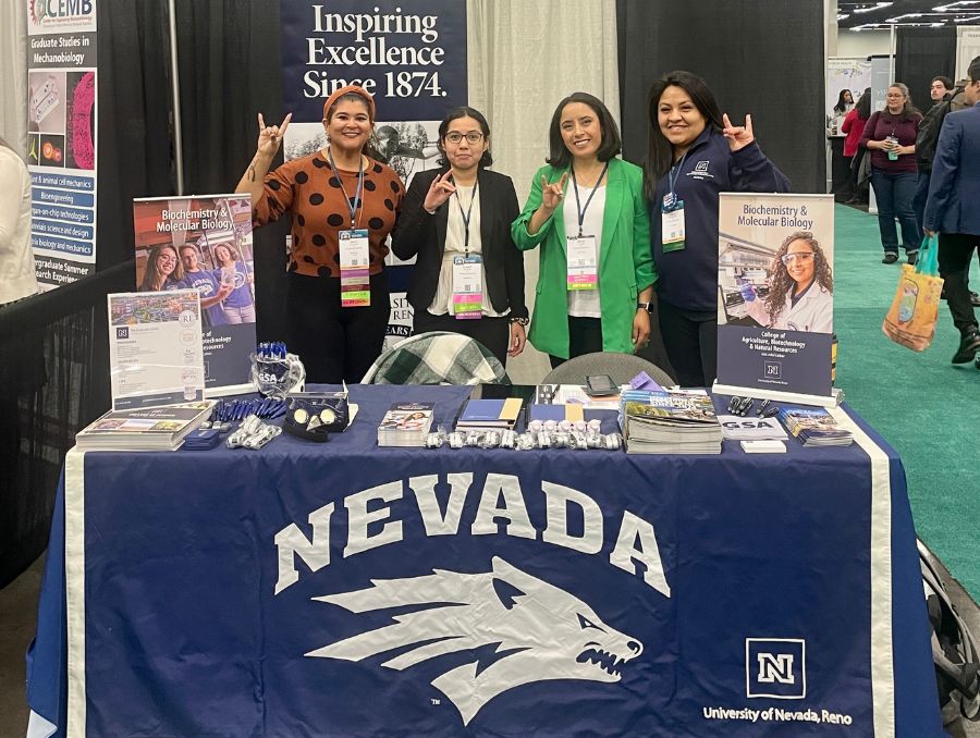 Four women stand at a University of Nevada, Reno booth at a conference.