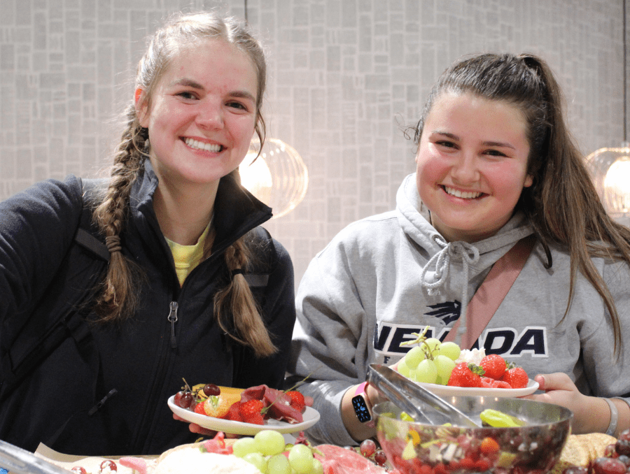 Two students smile and take a selfie while eating fruit. One student wears a Nevada sweatshirt.