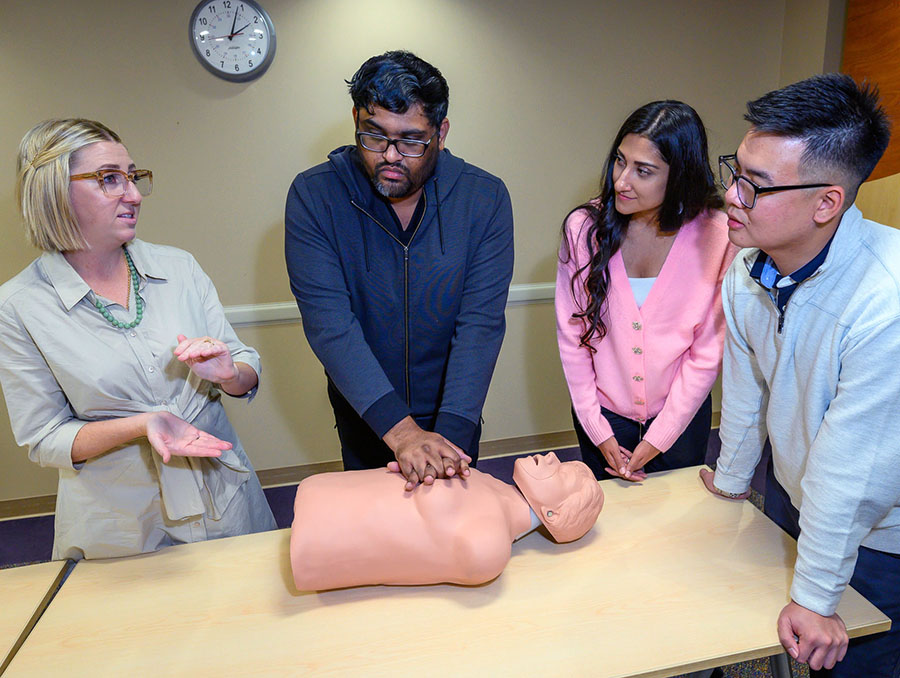 Four people practice CPR training on a human-like manikin on a conference room table