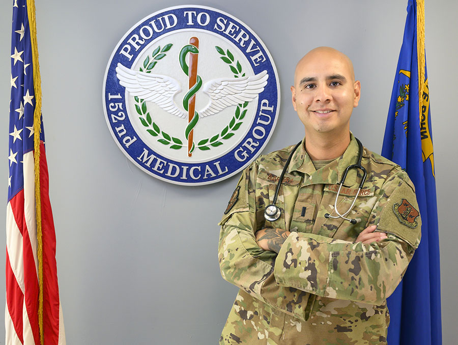 Nephtali Barrera poses in the hallway in his uniform next to a plaque that says "Proud to serve. 152nd Medical Group."