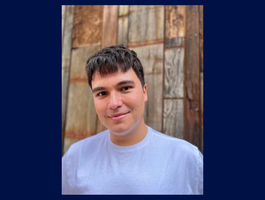 Carson Allen stands against a wooden background smiling at the camera