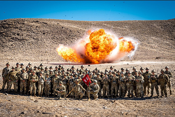 A large group in military uniforms stands in front of an explosion in Hawthorne, Nevada.