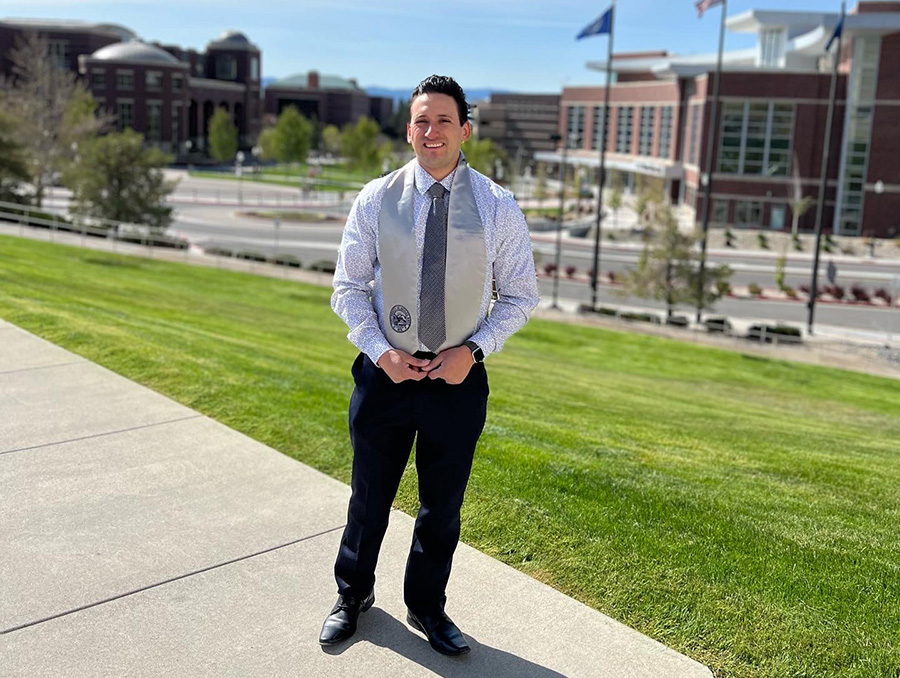 Gustavo Gomez stands outside at the University of Nevada, Reno wearing a graduation stoll.