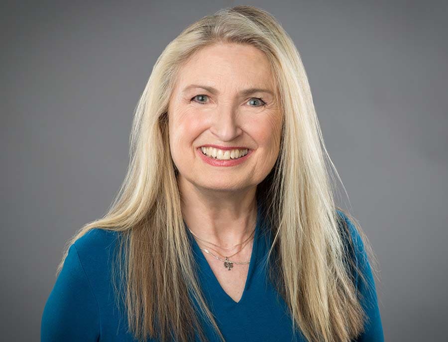 Headshot of Judith Sugar wearing a blue shirt and smiling.