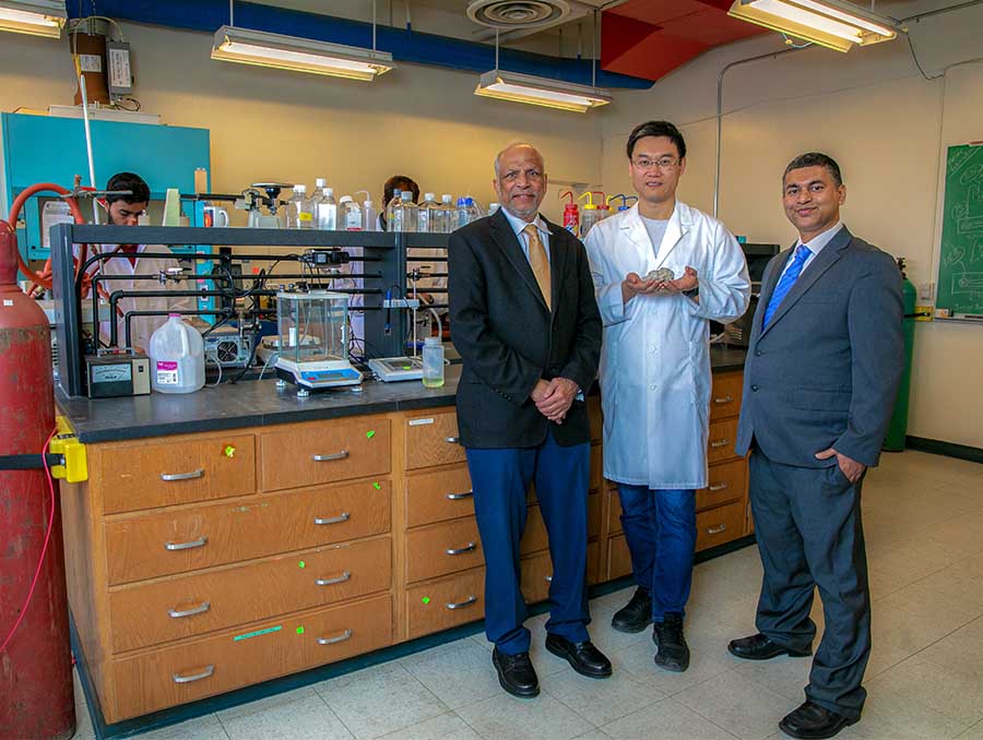 Misra, Chu and Menezes standing in a lab; Chu is holding a grayish rock.