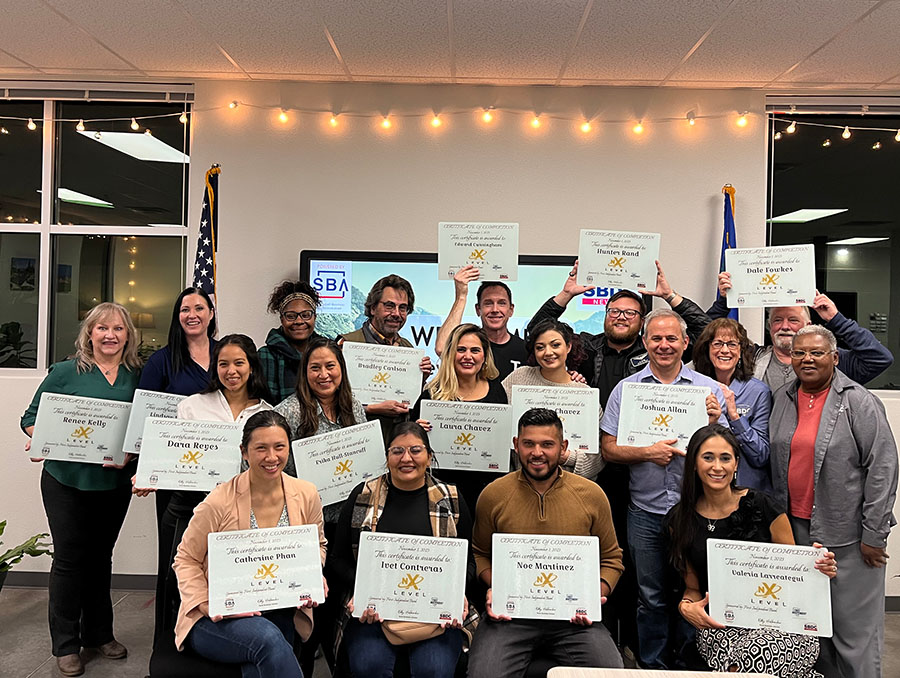 A group of people pose holding certificates of completion in a room with a white wall behind them.