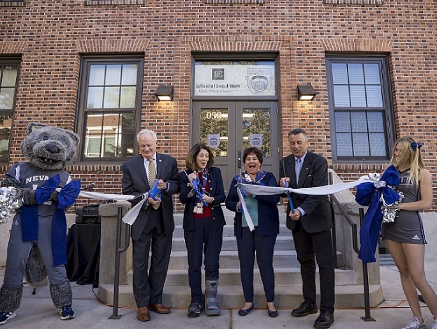 Provost Thompson, Dean Wichinsky, Regent Del Carlo and President Sandoval standing in front of building 058 cutting a ribbon held by Alphie the mascot and a cheerleader. 