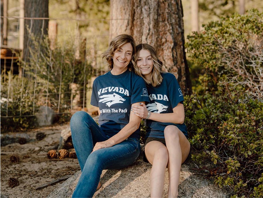 Two women wearing Wolf Pack shirts sitting under a tree.
