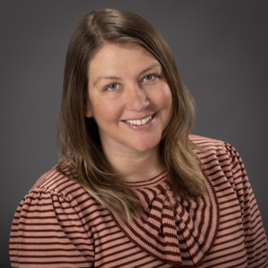 Angie Chase stands in a striped shirt smiling at the camera