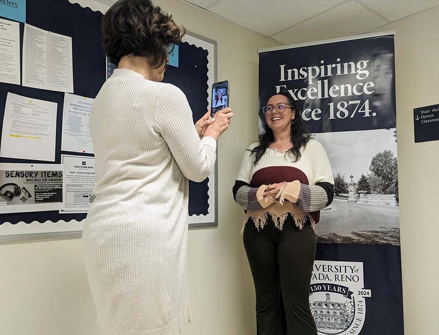 A smiling student being filmed by faculty for a TikTok video in front of a University 150 years celebration banner. 