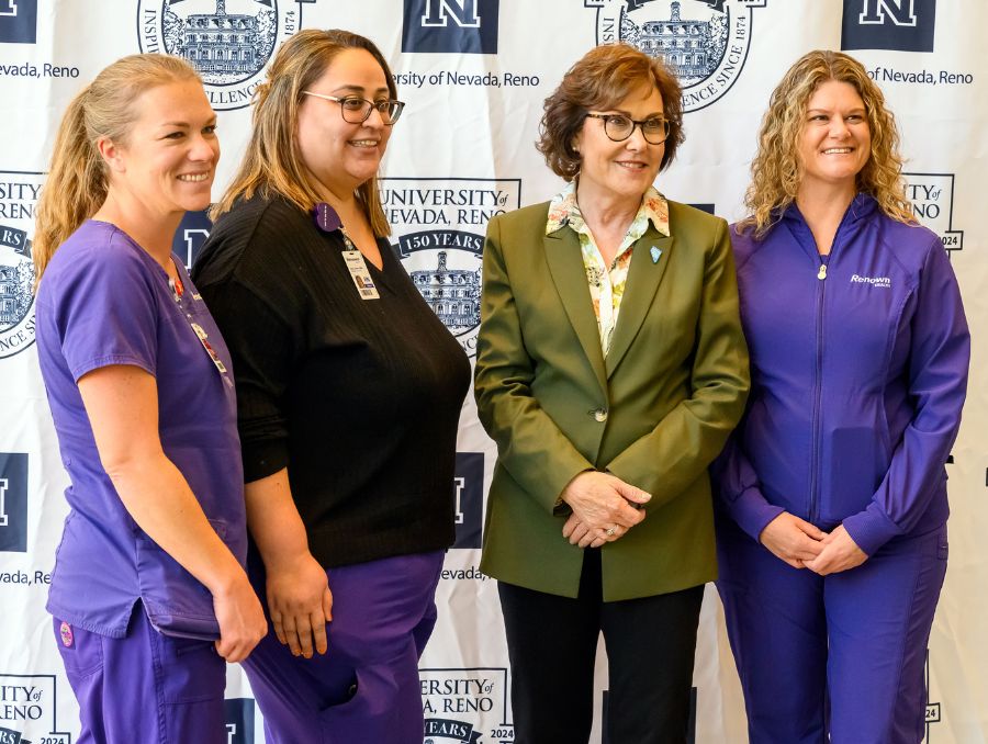 U.S. Sen. Jacky Rosen standing with three nurses in purple scrubs.