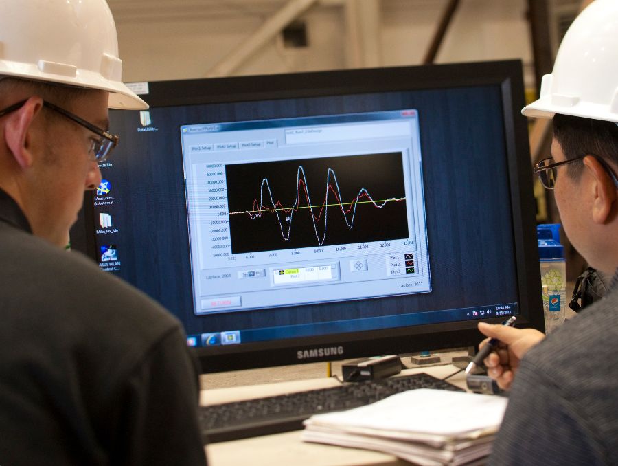 Two people in hard hats sit in front of a computer with seismology data on it.