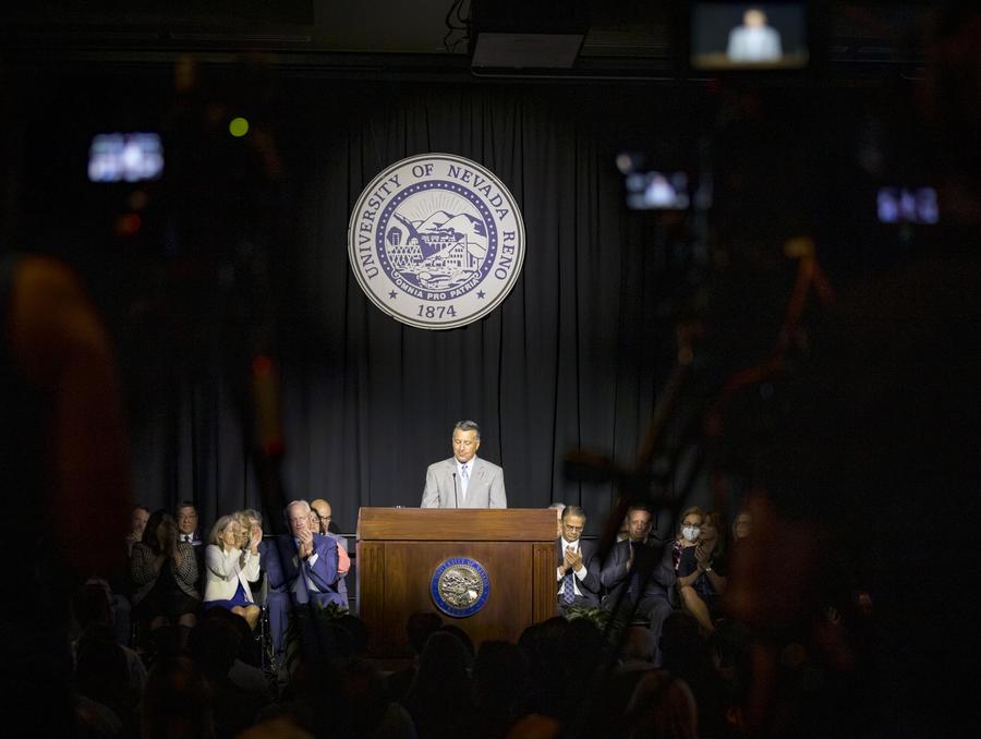 Brian Sandoval on stage with various regents, administrators, provosts and deans on stage with him clapping.