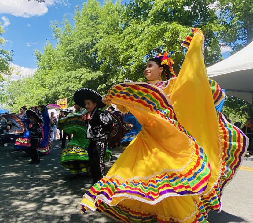 A woman in a bright yellow dress dances while others also in traditional dress watch.