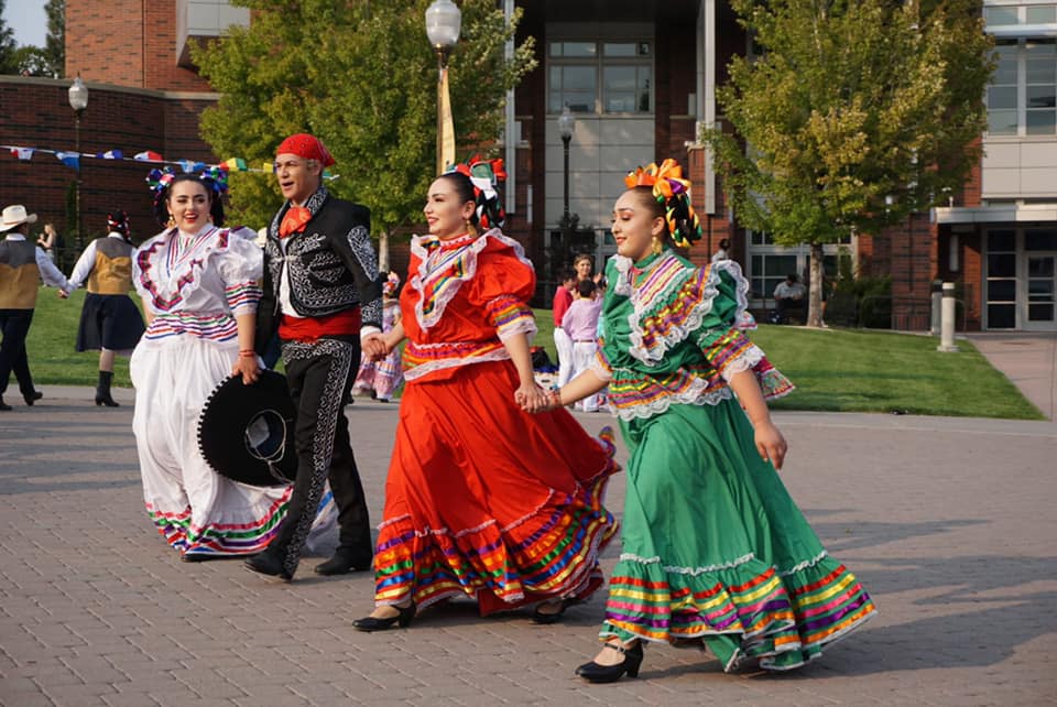 A group of dancers in brightly colored, traditional clothing dances on the Gateway Plaza in front of the Knowledge Center.