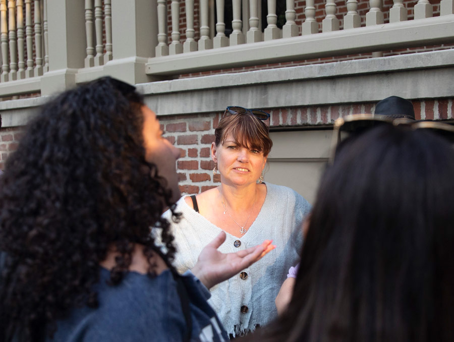 A woman, illuminated in golden hour light, stands in front of Morrill Hall, with two students in the foreground facing her and speaking with her.