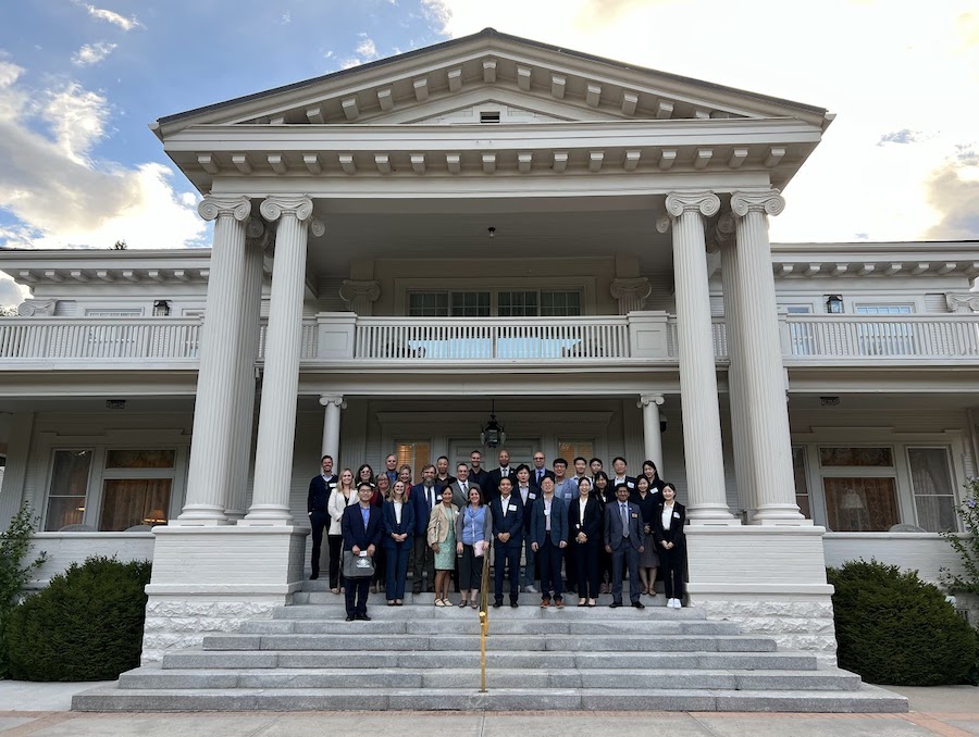 A large group of about 20-30 individuals in professional clothing smile on the steps of the Nevada Governor's Mansion