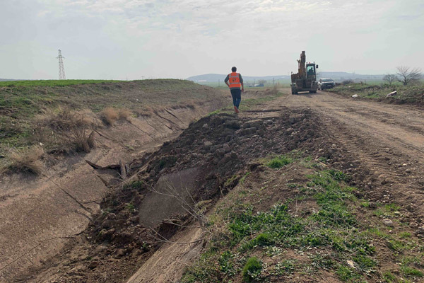 A man walks away from a displaced drainage ditch toward a backhoe.