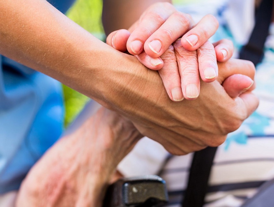 Hands of a person helping an older woman in a wheelchair.