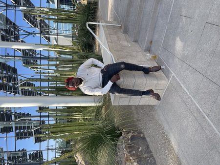 Jay Jordan in dress pants and sweater sits on concrete steps