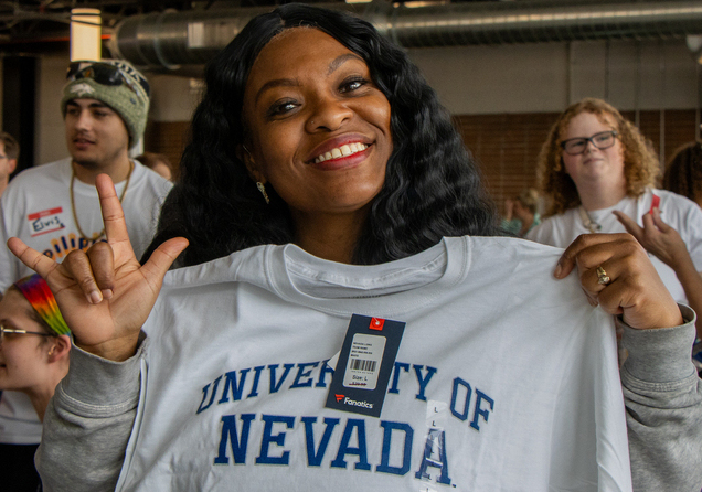 A woman smiling and holding a University T-shirt.