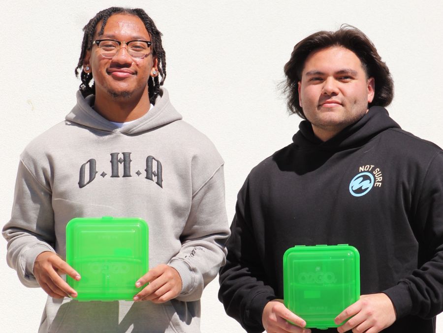Two students posing holding up reusable green boxes.