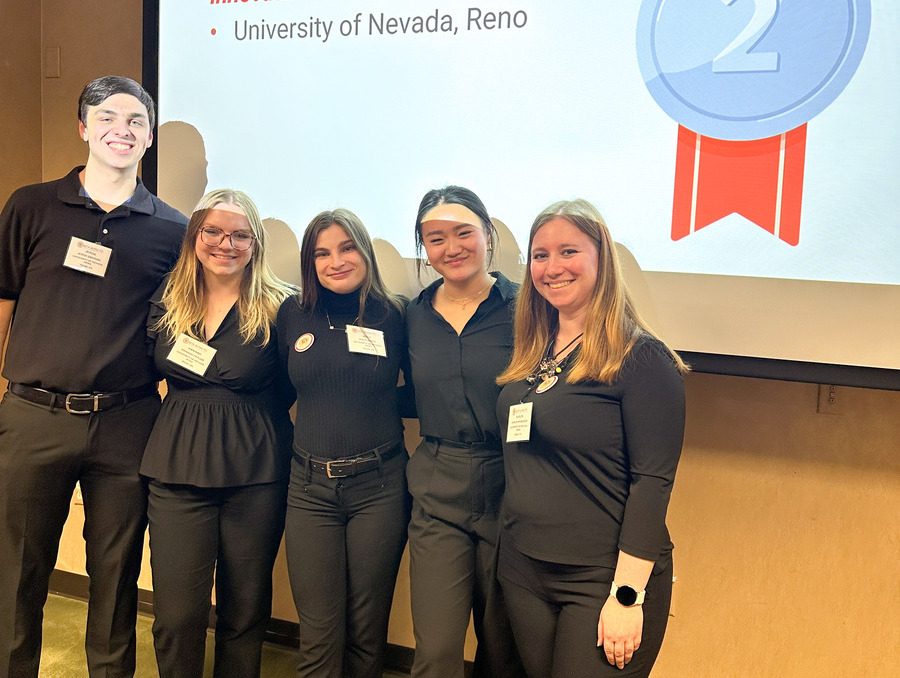 Five people in business attire standing in front of a power point presentation.