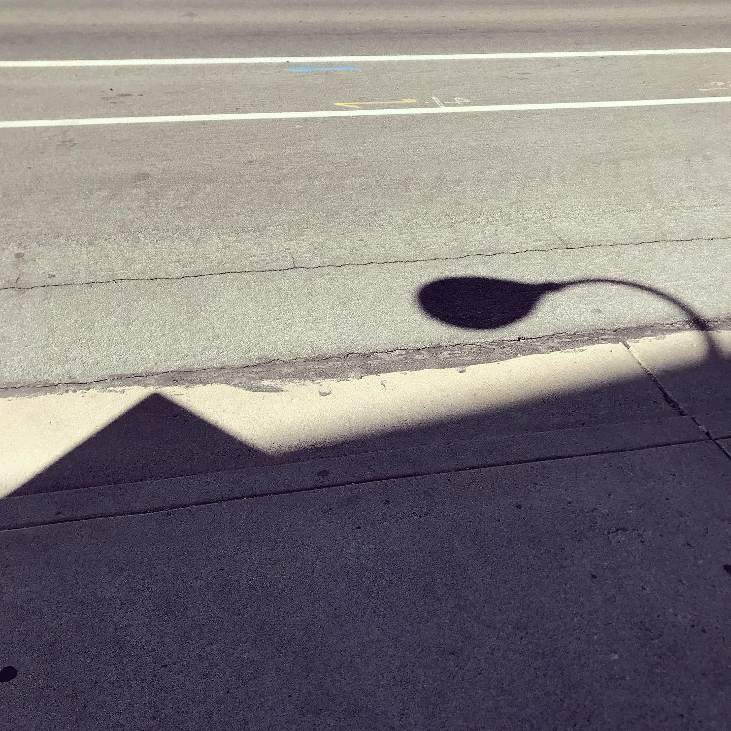 The shadow of a light pole and building cast on a street, emulating a pyramid landscape.