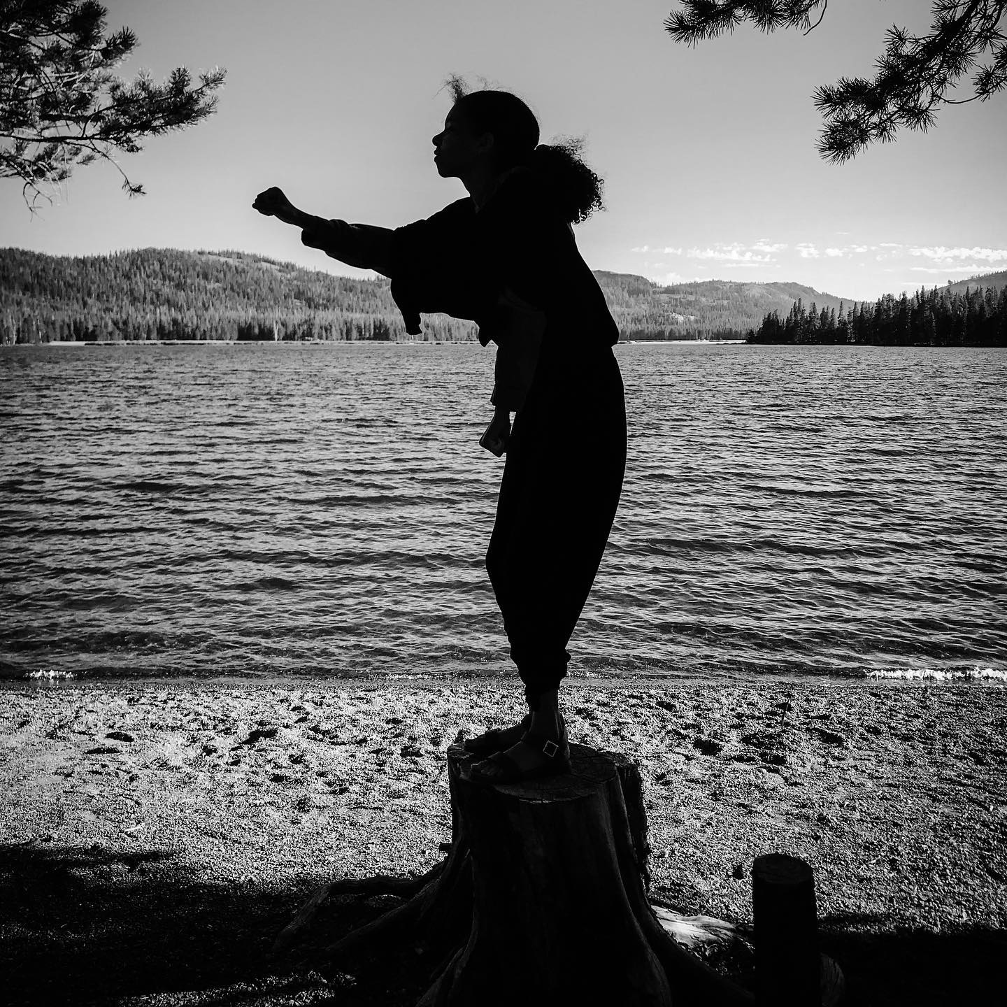 A dancer stands on the edge of a lake dancing, in black and white.